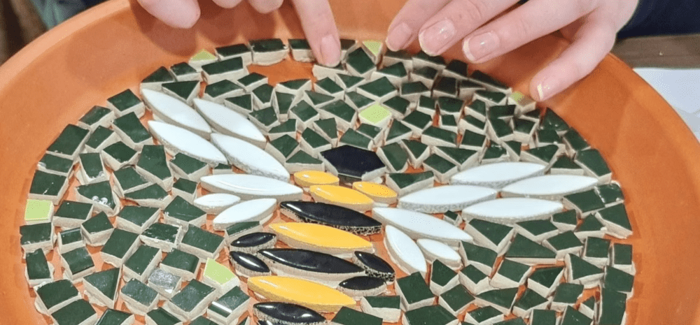 Hands handling and organising mosaic pieces to create a bee shaped image.