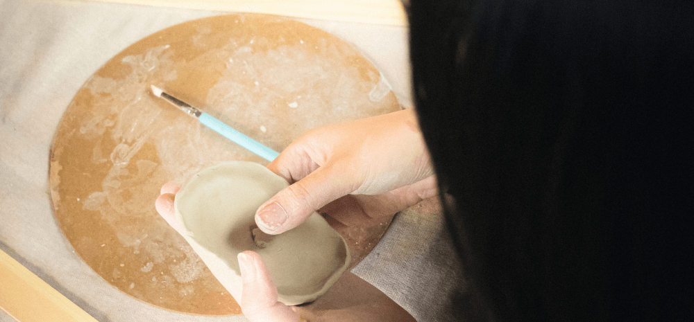 A person holding a piece of clay, creating a vessel shaped object.