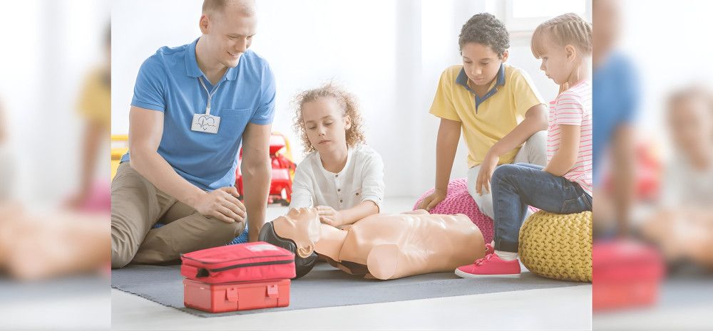 Trainer and group of children practising first aid on a manequin