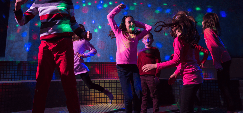 Six children dancing in a dark room with disco lights.
