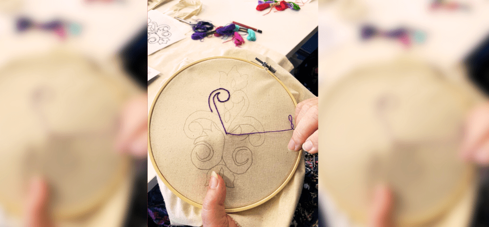 A woman working on her embroidery using equipment including hoop, canvas, patterns and colourful threads.
