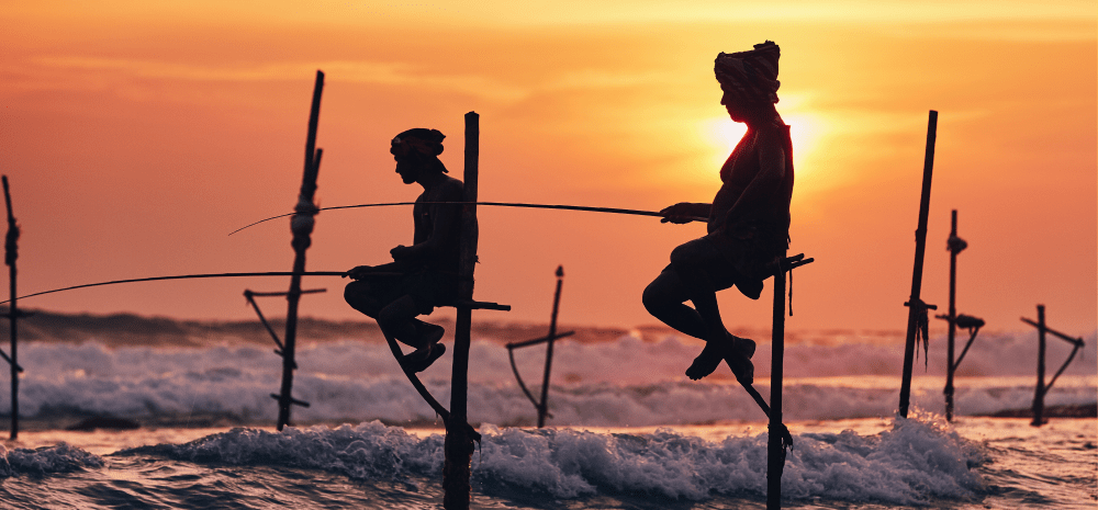 Silhoutte of figures fishing on wooden platforms by the coast.