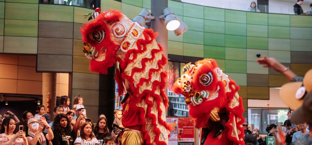 Traditional lion dance with two lions rising above a crowd in the library.