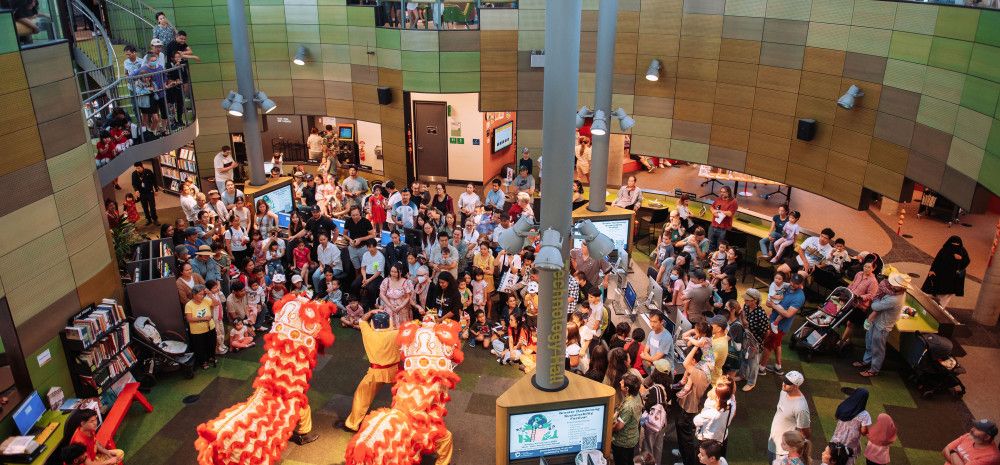 Traditional lion dance at Springvale Library viewed from above, with a crowd of people watching.