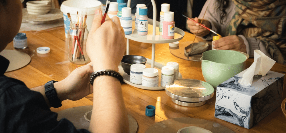 People painting ceramics on a table with painting supplies. 
