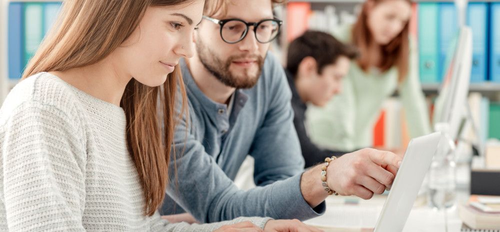 Students studying in a library with a laptop.