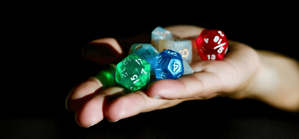 A hand holds several colorful multi‑sided tabletop gaming dice against a dark background.