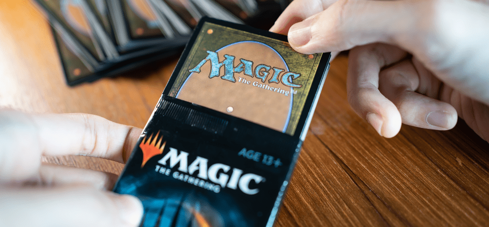 A close up image of hand opening a Magic the Gathering booster pack on a wooden table. 