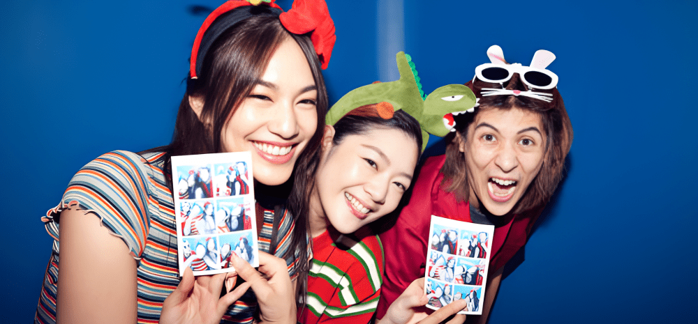Three women smiling and holding photos taken in a photobooth.