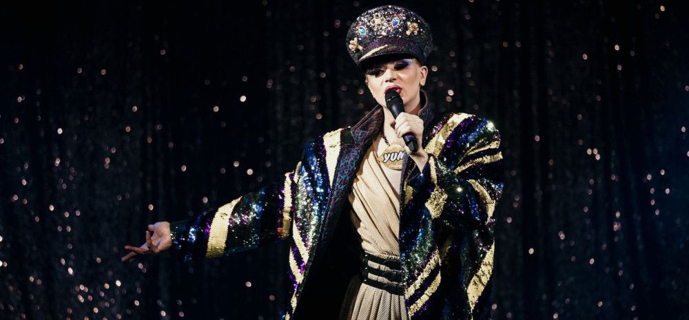 Drag performer on stage with microphone in hand.