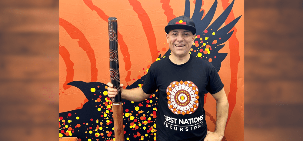Person holding a decorated didgeridoo against a vibrant Indigenous-style backdrop.