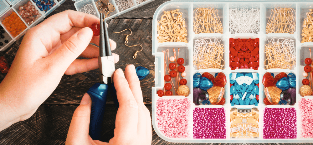 Someone using pliers to create bead and wire jewellery next to a sorted bead container. 