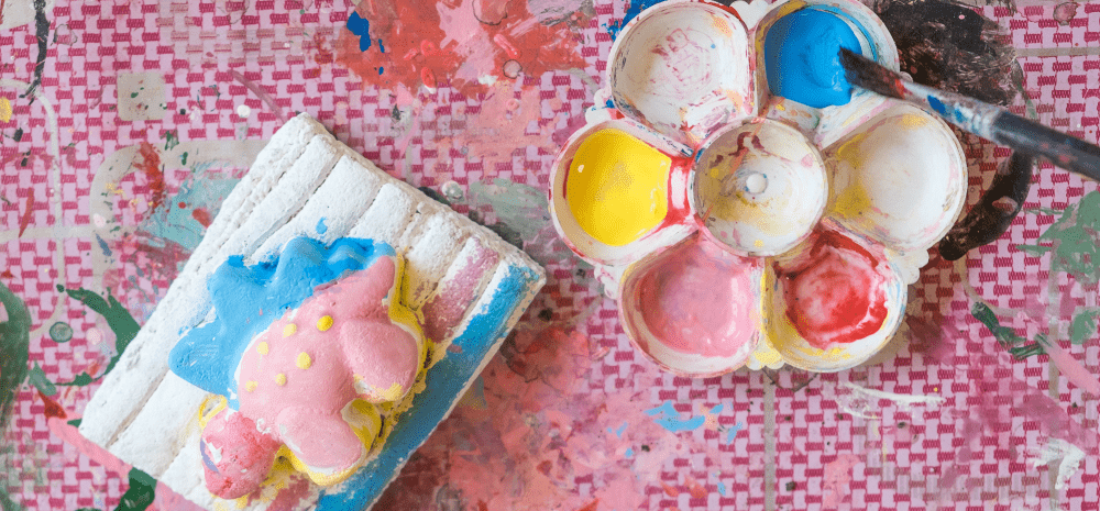 A colourful plaster dinosaur figurine displayed on a pink surface next to a palette with paint samples.