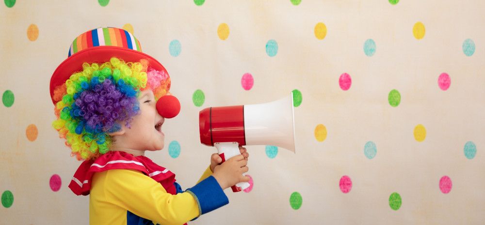A child dressed as a clown yelling into a megaphone.