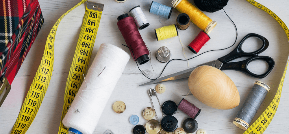 Sewing items on a table, including measuring tape, scissors, thread, pin and buttons.
