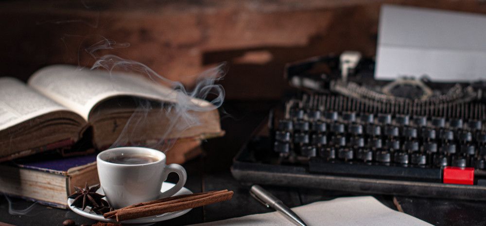 Books, tea and spices laid out on a table with pen, paper and a typewriter.