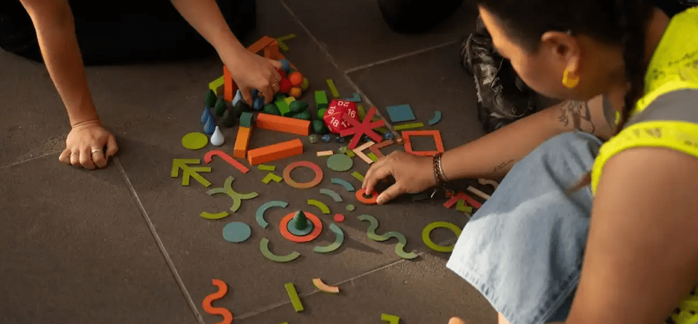 People collaboratively explore colourful geometric shapes and building pieces spread across a floor.