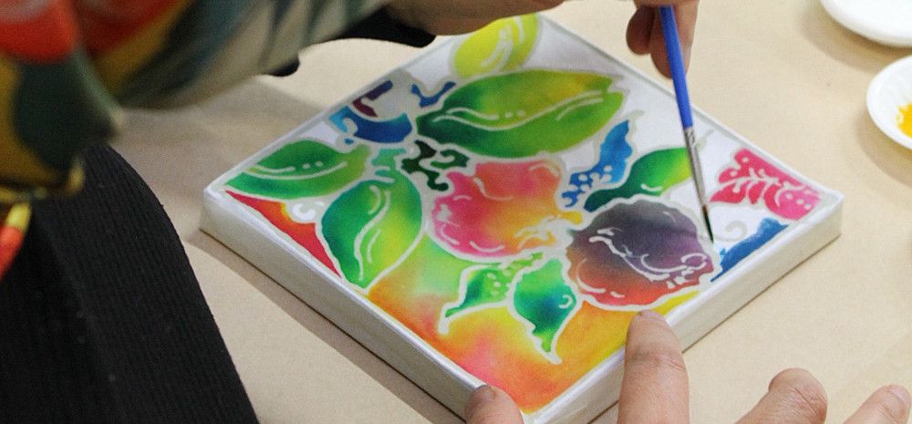 A person holding a paintbrush and painting a colourful image on batik.