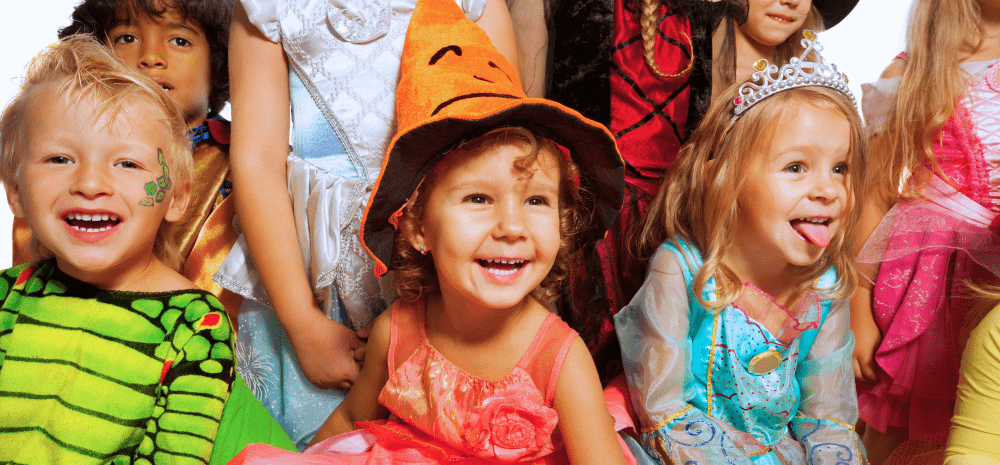 Children dressed in colourful Halloween and fairy tale costumes smiling together at a toddler event.