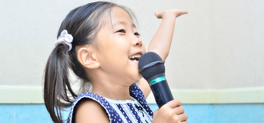 A child holding a microphone with one hand raised. 