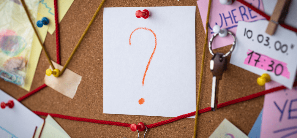 A question mark on a piece of paper pinned to a cork board with strings, keys and papers pinned around it. 