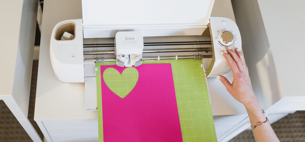 A person creating love heart shapes out of a pink coloured material on a Cricut machine.