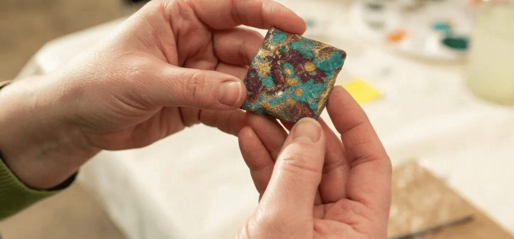 Hands holding a colourful, painted, square stone. 