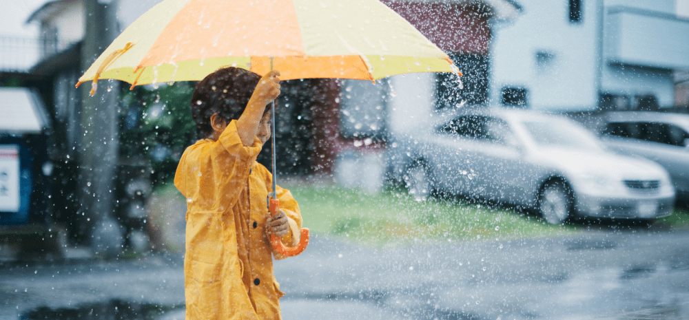 A child in a yellow raincoat holding an umbrella in the rain.