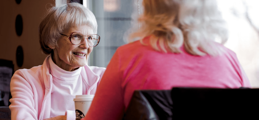 A older woman smiling at another woman over coffee. 