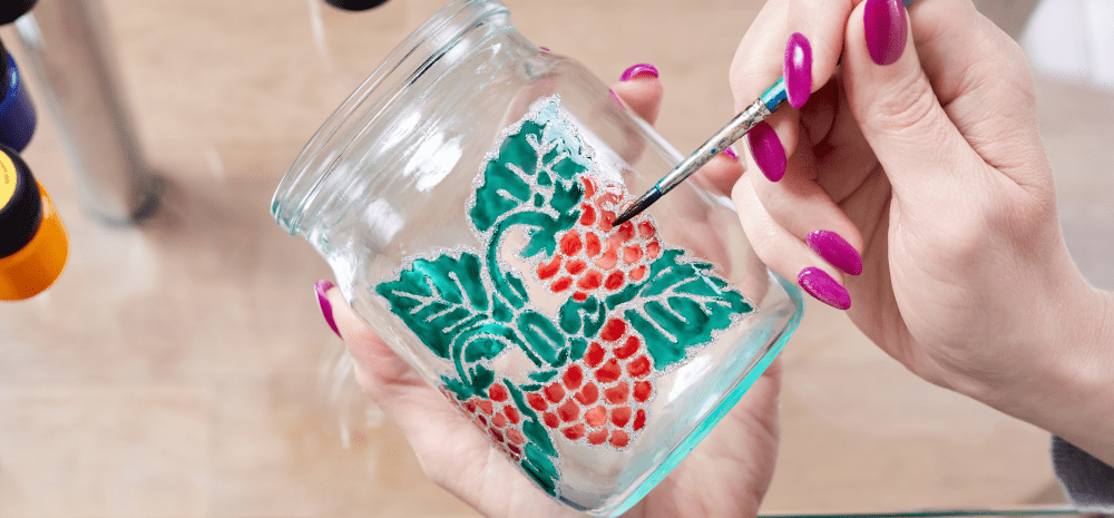 Hands painting raspberries on a glass jar. 