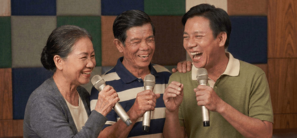 Three older people, a woman and two men, singing karaoke together and having fun.