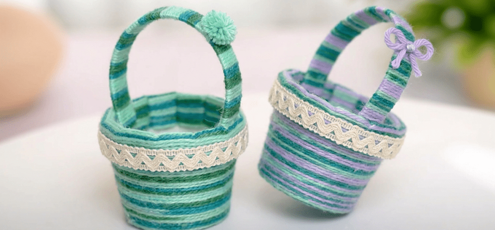 Two small woven baskets wrapped in green, blue and purple yarn with decorative trim and handles.