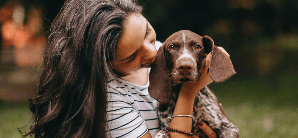 A woman gently holds a brown and white dog outdoors, with the dog looking directly at the camera.