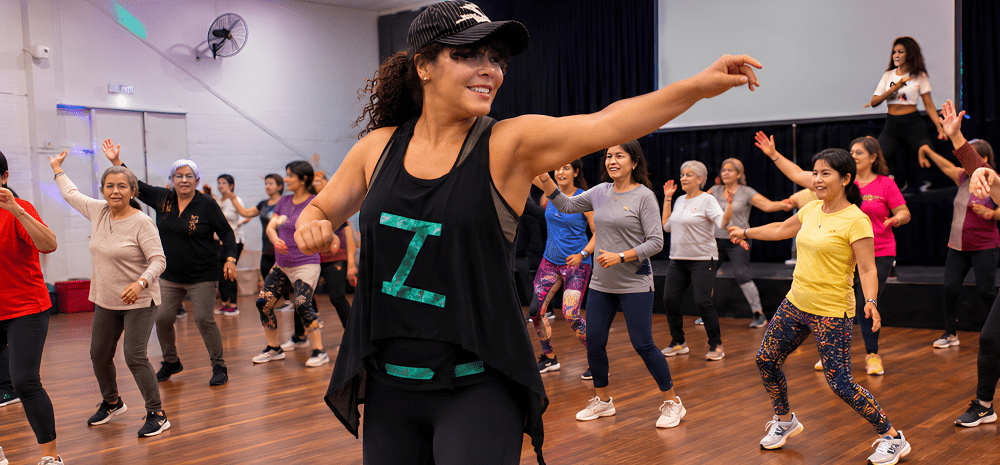 A woman teaching Zumba class, surrounded by her students, mostly older ladies. 