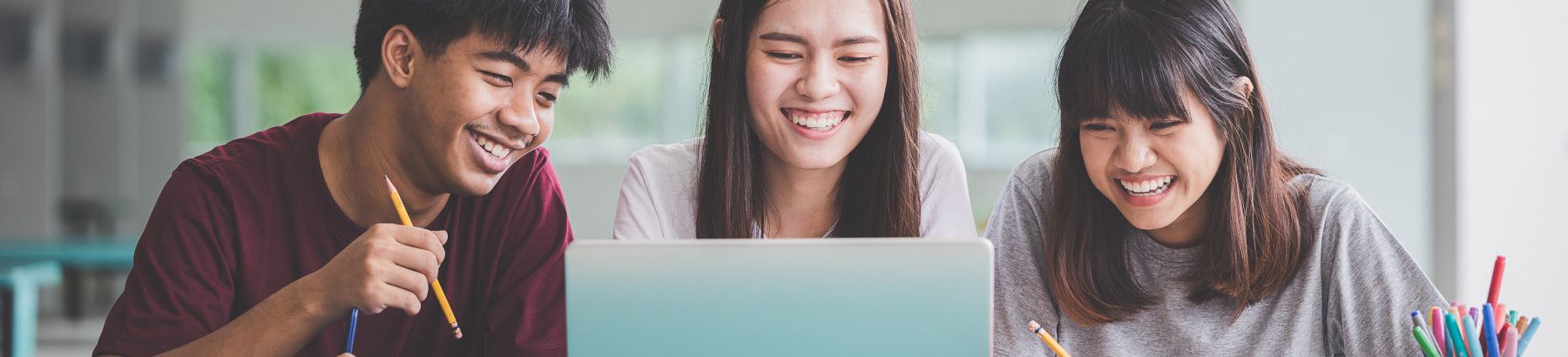 Three students smiling with a laptop.