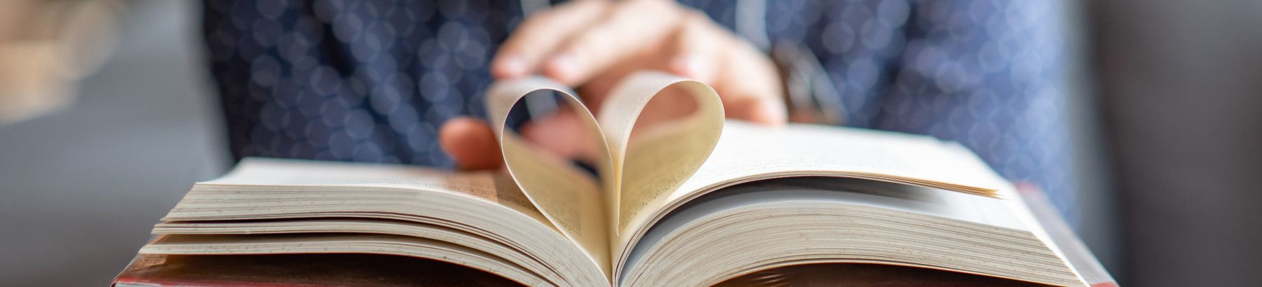Closeup of a person's hands holding a book with pages folded into a heart shape.