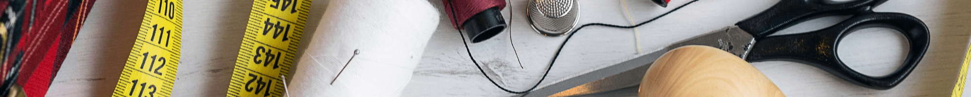 Sewing items on a table, including measuring tape, scissors, thread, pin and buttons.