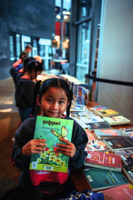 Child holding a library book. There are other children in the background and library books on the table.
