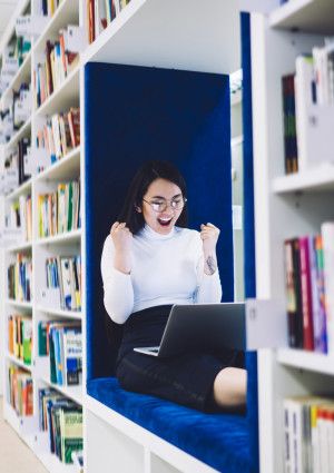 Happy student with laptop in the library.