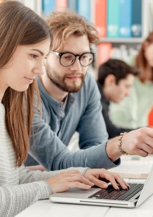 Students studying in a library with a laptop.